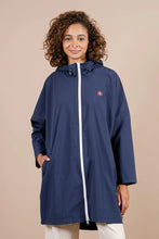 Load image into Gallery viewer, A woman standing outdoors wearing a navy blue rain cape with a visor, featuring white zippered side panels and a logo on the chest.